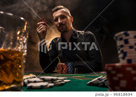 Man is playing poker with a cigar and a whiskey. A man winning all the chips on the table with thick cigarette smoke. 96818694