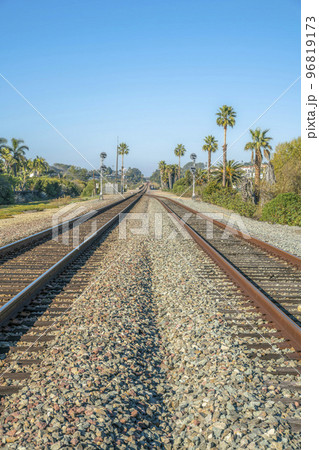 Rusty railway tracks on rocky road along homes against palm trees and blue sky Rusty railway tracks on rocky road along homes against palm trees and blue sky 96819173