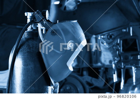Welding equipment in a car repair station, helmet hanging on a gas tank, no people 96820106