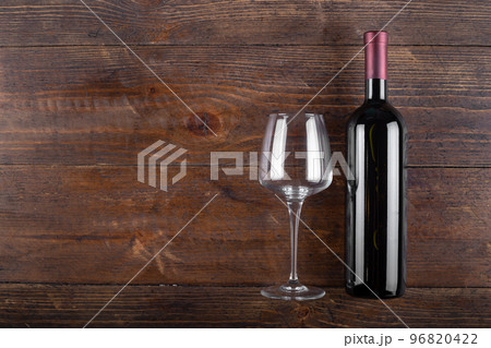 Bottle of red wine and an empty glass on a wooden background. 96820422