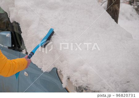 Caucasian woman brushing a car from freshly fallen snow. Caucasian woman brushing a car from freshly fallen snow. 96820731