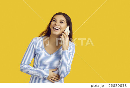 Portrait of excited woman touching her stomach with hand talking on phone isolated on yellow colored background with blank space Portrait of excited woman touching her stomach with hand talking on phone isolated on yellow colored background with blank space 96820838
