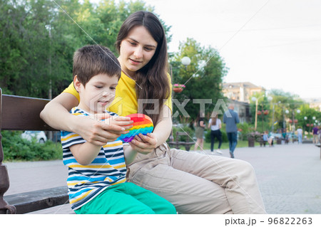 Mom and baby boy 4 years old play with a colored trendy toy Pop it in the park in nature. Antistress sensitive toy or reusable bubble wrap. Trend 2021 96822263