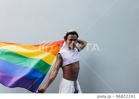 Young stylish man walking at grey wall raising hands with LGBT flag 96822291