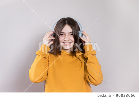A teenage girl with long dark hair smiles and laughs in a bright orange hoodie in headphones listening to music with place for text and copy space. A teenage girl with long dark hair smiles and laughs in a bright orange hoodie in headphones listening to music with place for text and copy space. 96823666
