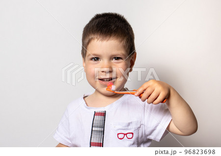 A little boy holds an orange toothbrush with toothpaste. The child brushes his teeth, prevention of tooth decay A little boy holds an orange toothbrush with toothpaste. The child brushes his teeth, prevention of tooth decay 96823698