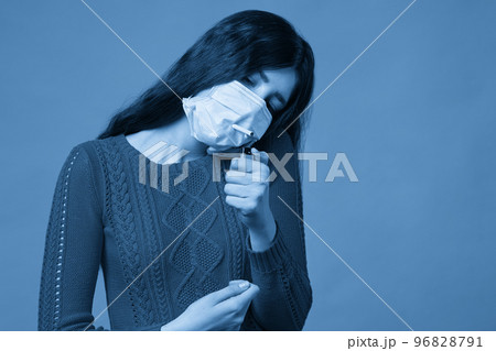 Young girl wearing medical protective mask lights up, holding a cigarette in her mouth through the mask Young girl wearing medical protective mask lights up, holding a cigarette in her mouth through the mask 96828791