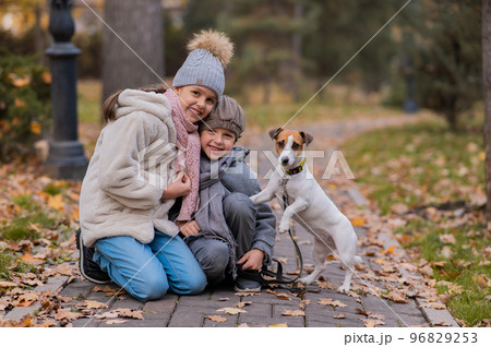 Caucasian boy and girl posing sitting on sidewalk with jack russell terrier dog in park in autumn. Caucasian boy and girl posing sitting on sidewalk with jack russell terrier dog in park in autumn. 96829253