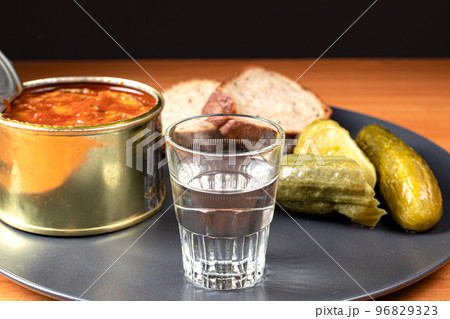 Drinks and snacks. A glass of vodka, sprats, bread and pickles. 96829323