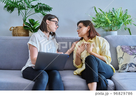 Female psychologist and middle aged woman patient sitting together on couch in office Female psychologist and middle aged woman patient sitting together on couch in office 96829786