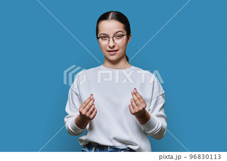 Teenage girl making money gesture, rubbing her fingers, on blue background 96830113