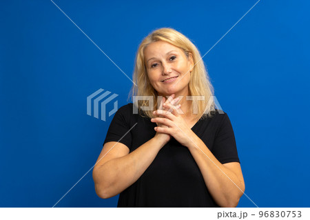 Photo portrait of a cute caucasian woman with her hands together looking impressed in admiration, dressed in a black t-shirt. Isolated on blue studio background. 96830753