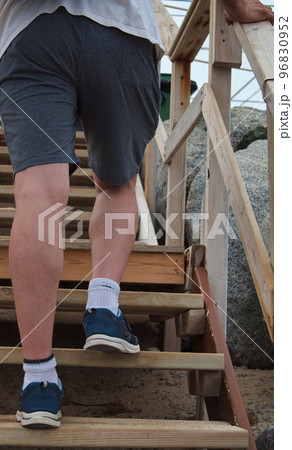 view from behind of the feet of a man climbing a wooden ladder on the beach 96830952