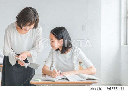 夏期講習で教科書を見ながら教える塾講師・先生と疑問を質問する小学生・中学生・高校生の生徒（子供） 96833131