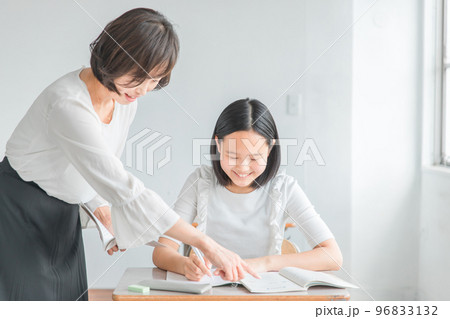 教科書を見ながら教える塾講師・先生と質問する笑顔の小学生・中学生・高校生の生徒（女の子） 96833132