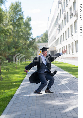 Old happy man in graduation gown jumping outdoors and holding diploma. Vertical. 96838403