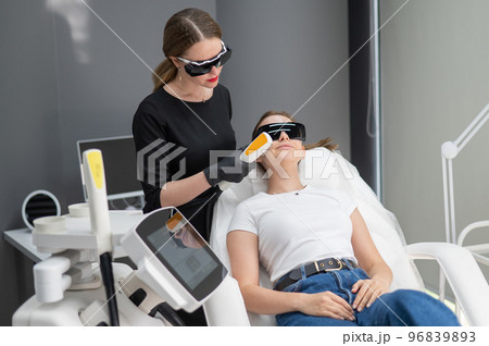 Young caucasian woman in goggles on photorejuvenation procedure. Doctor cosmetologist with a female patient. 96839893