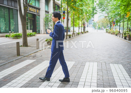 コーヒーを片手にオフィス街を歩くビジネスマン 96840095