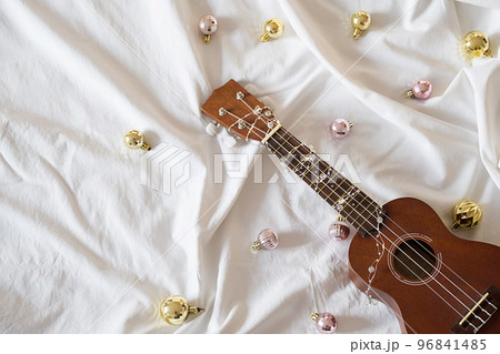 Ukulele guitar, Christmas balls and garland lights on white. Winter festive composition. Ukulele guitar, Christmas balls and garland lights on white. Winter festive composition. 96841485