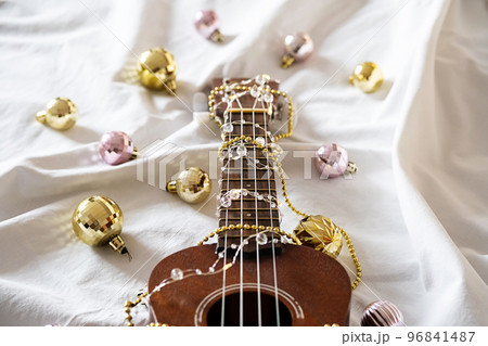 Ukulele guitar, Christmas balls and garland lights on white. Winter festive composition. Ukulele guitar, Christmas balls and garland lights on white. Winter festive composition. 96841487