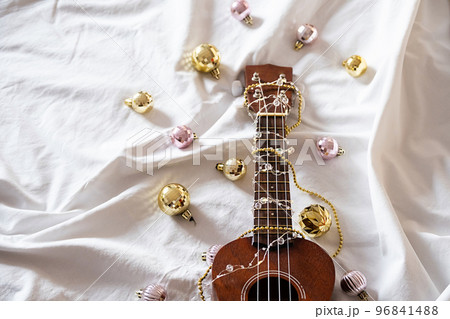 Ukulele guitar, Christmas balls and garland lights on white. Winter festive composition. Ukulele guitar, Christmas balls and garland lights on white. Winter festive composition. 96841488