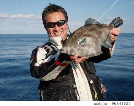 快晴の海をバックに釣り上げられた大型のウマズラハギを持つ釣人。 96841626