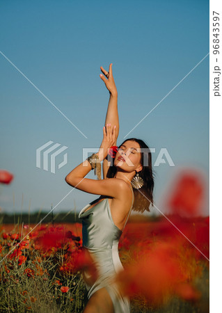Portrait of a girl in a dress on a poppy field at sunset 96843597