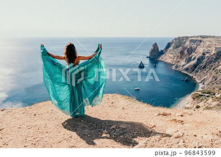 Side view a Young beautiful sensual woman with black hair in a long mint dress posing on a beach with calm sea bokeh lights on sunny day. Girl on the nature on blue sky background. Fashion photo 96843599