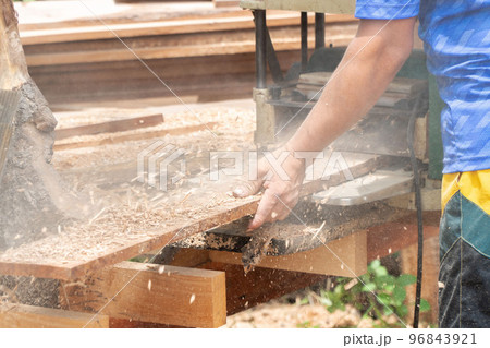 Joiner, Man's hand scouring a wooden board on a thickness machine in garden. Carpenter working with electric planer on wooden beam, plank.DIY concept 96843921