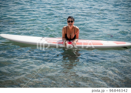 Woman sap sea. Sports girl on a surfboard in the sea on a sunny summer day. In a black bathing suit, he lies on a sap in the sea. Rest on the sea. Woman sap sea. Sports girl on a surfboard in the sea on a sunny summer day. In a black bathing suit, he lies on a sap in the sea. Rest on the sea. 96846342