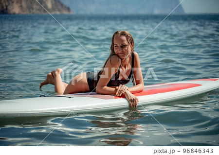 Woman sap sea. Sports girl on a surfboard in the sea on a sunny summer day. In a black bathing suit, he lies on a sap in the sea. Rest on the sea. Woman sap sea. Sports girl on a surfboard in the sea on a sunny summer day. In a black bathing suit, he lies on a sap in the sea. Rest on the sea. 96846343