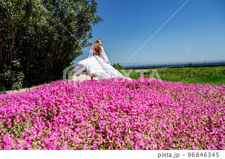 a beautiful woman in a white flowing long dress stay near a beautiful field with pink flowers rear view a beautiful woman in a white flowing long dress stay near a beautiful field with pink flowers rear view 96846345