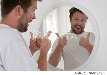 Man trying to encourage himself showing thumb up looking in mirror. Man trying to encourage himself showing thumb up looking in mirror. 96847479