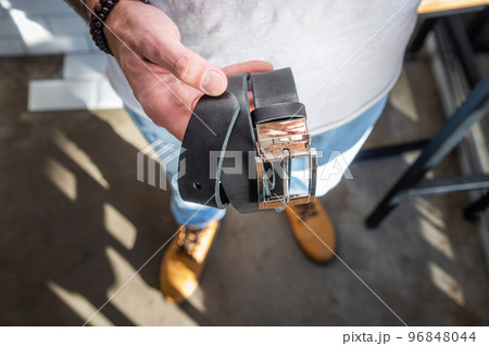 Man holds handmade black leather belt in his hand. Close-up, top view. Fashion and stylish accessories Man holds handmade black leather belt in his hand. Close-up, top view. Fashion and stylish accessories 96848044
