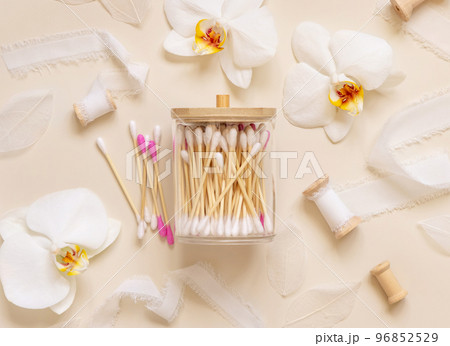 Bamboo cotton buds in a jar near white orchid flowers on light beige. Eco friendly skincare product 96852529