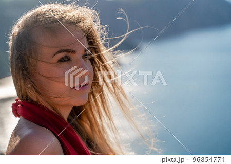 A woman in a red flying dress fluttering in the wind, against the backdrop of the sea. 96854774
