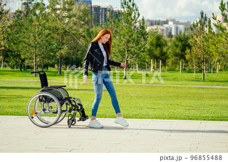 redhaired ginger woman making first steps after long recovery.she walking without her wheelchair in spring park redhaired ginger woman making first steps after long recovery.she walking without her wheelchair in spring park 96855488