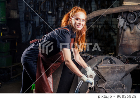 redhaired ginger young european feminist woman wearing leather apron working blacksmith workshop.small business strong and independent concept 96855928