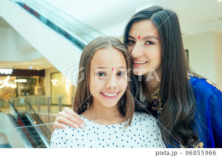 Portrait of a young indian woman wearing blue sari and gold bracelet having fun with her cute daughter in shopping mall,escalator background.red religious dot on forehead 96855966