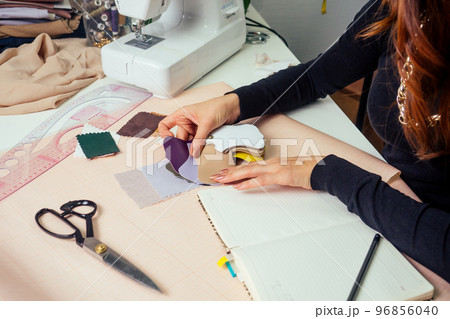 beautiful seamstress with long hair writes in a notebook. the tailor creates a collection of outfits. young woman designer clothes working with leather 96856040