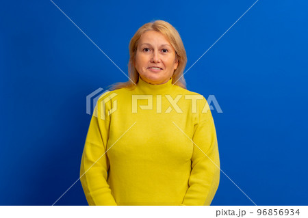Beautiful blonde woman in yellow sweater looking to side to side with smile on face isolated over blue background, natural expression. Laughing confident Beautiful blonde woman in yellow sweater looking to side to side with smile on face isolated over blue background, natural expression. Laughing confident 96856934