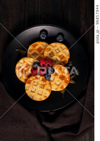Small round waffles with berries on dark background, flat lay Small round waffles with berries on dark background, flat lay 96857944