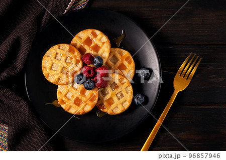 Small round waffles with berries on dark background, flat lay Small round waffles with berries on dark background, flat lay 96857946