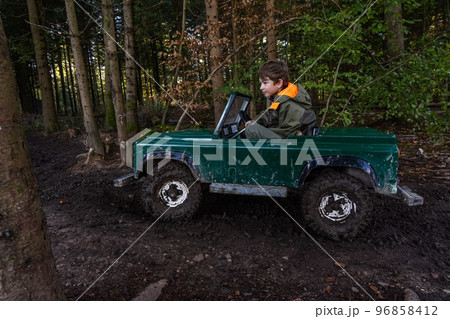 A Teen ride in an open iron children's car. Extreme form of entertainment for children. The boy drives through the mud in the forest A Teen ride in an open iron children's car. Extreme form of entertainment for children. The boy drives through the mud in the forest 96858412
