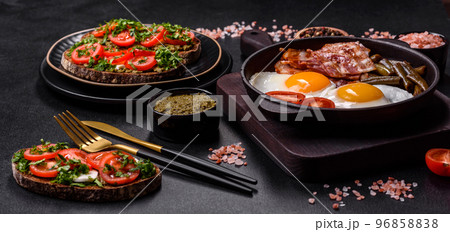 Tasty breakfast consists of eggs, bacon, beans, tomatoes, with spices and herbs Tasty breakfast consists of eggs, bacon, beans, tomatoes, with spices and herbs 96858838