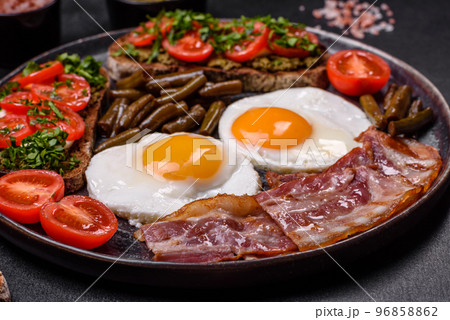 Tasty breakfast consists of eggs, bacon, beans, tomatoes, with spices and herbs Tasty breakfast consists of eggs, bacon, beans, tomatoes, with spices and herbs 96858862