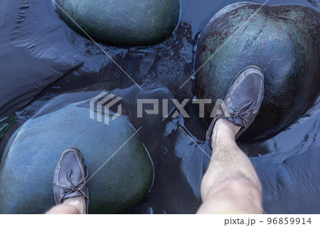 male feet in top siders on green stones over water male feet in top siders on green stones over water 96859914