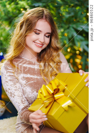 a beautiful woman in a shiny dress with a gift by the christmas tree. 96860522