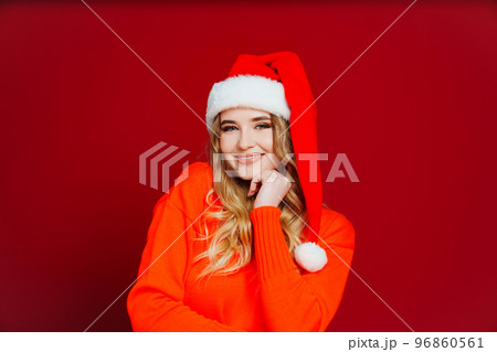 a cute beautiful woman in a Santa Claus hat on a red background. a cute beautiful woman in a Santa Claus hat on a red background. 96860561