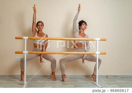 Near the barre, in the choreographic hall, two women in a beige top and leggings are engaged. 96860617